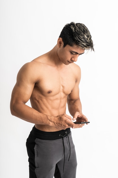 Asian young man with muscular body holding a smartphone with two hand typing stand facing forward and look at a phone