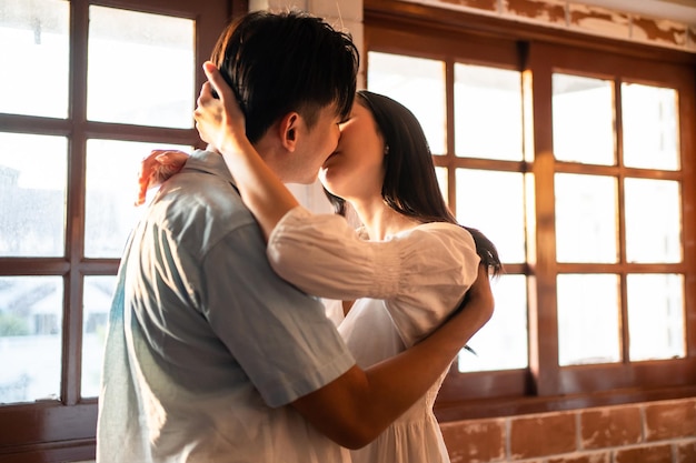 asian young man and woman kissing each other in living room at home attractive romantic new marriage couple male and female spend time celebrate anniversary and valentines day together in house