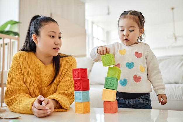 Asian young mom playing with her child in toys in the living room at home