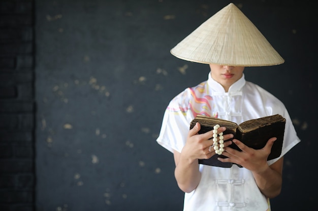 Asian young monk in hat on black wall background