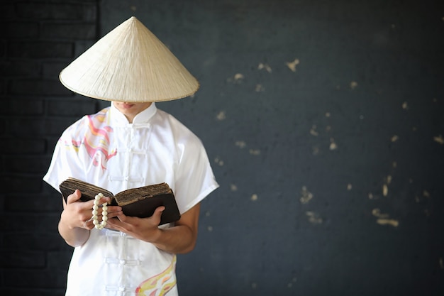 Asian young monk in hat on black wall background