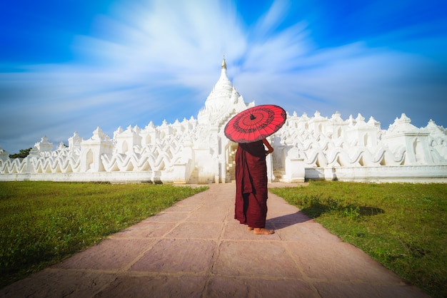 Фото Азиатский молодой монах, держащий красные зонтики в mya thein tan pagoda в mingun