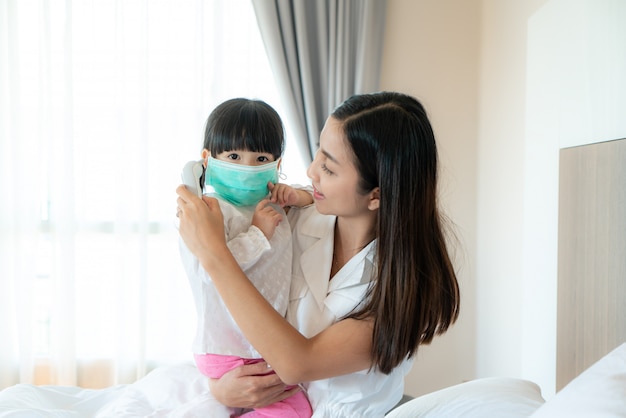 La giovane madre asiatica che controlla la temperatura di misura della sua piccola figlia malata si sente come la febbre o l'influenza in camera da letto a casa.