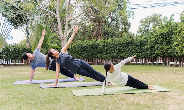 Asian young mother, father practicing doing yoga exercises with child daughter outdoors in meditate pose together in nature a field garden park, family kid sport and exercises for healthy lifestyle