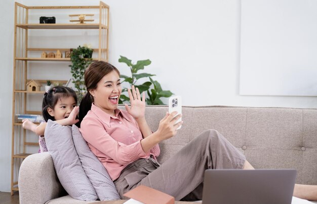 アジアの若い母親と娘は、一緒に楽しんでいる家族とビデオ通話会議をしています