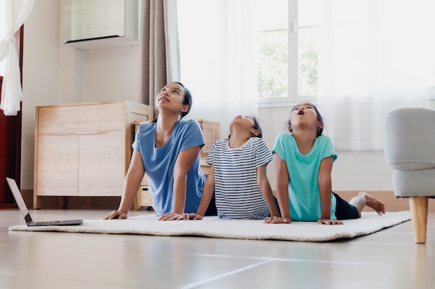 Giovane madre asiatica e le sue figlie che fanno yoga esercizio di stretching insieme a casa. genitori e figli si allenano per essere forti e mantenere la salute fisica e il benessere nella routine quotidiana.