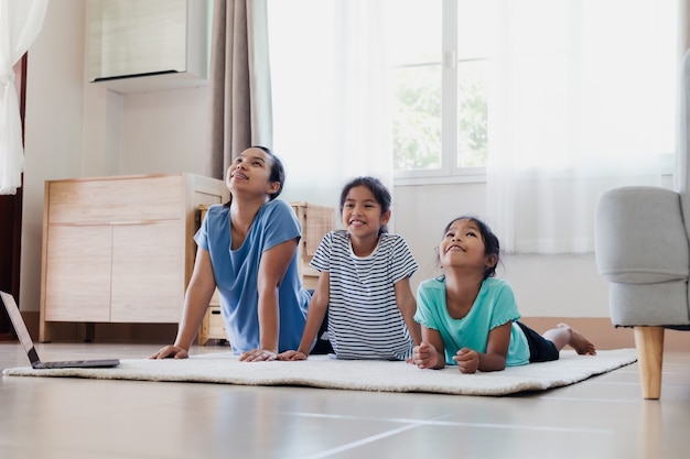 Giovane madre asiatica e le sue figlie che fanno yoga esercizio di stretching insieme a casa. genitori e figli si allenano per essere forti e mantenere la salute fisica e il benessere nella routine quotidiana.