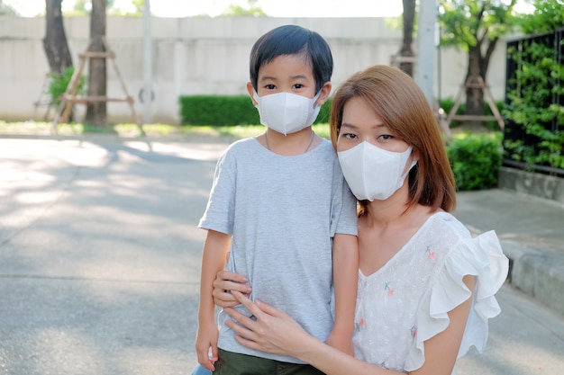 Giovane madre asiatica che indossa la maschera protettiva pm2.5 per suo figlio ad all'aperto