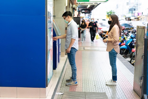 Asian young people wearing face masks stand in line to using ATM and self service machines