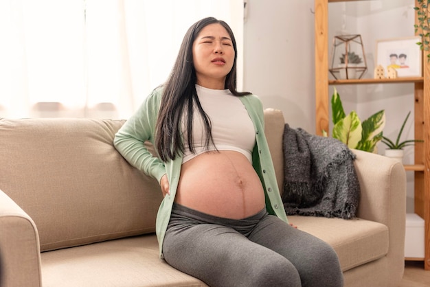 Asian young pregnant woman with big belly has backache back pain on sofa