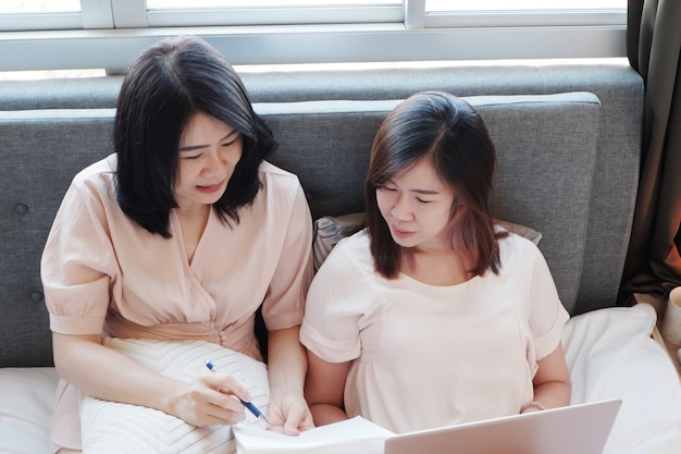 asian young sisters laying on bed and online working on laptop