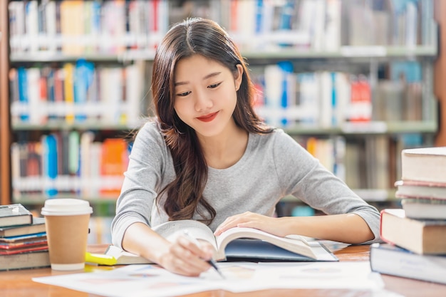 Asian young student in casual suit reading and doing homework in library of university or colleage