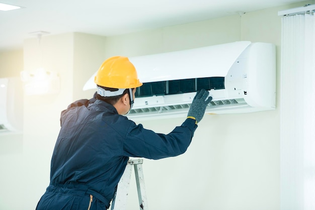 An Asian young Technician service man wearing blue uniform checkingProfessional air conditioner installer maintaining modern indoor air conditioner space for text