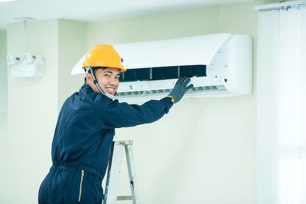 An Asian young Technician service man wearing blue uniform checkingProfessional air conditioner installer maintaining modern indoor air conditioner space for text