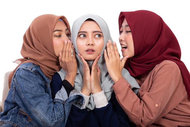 彼女の友人が座っている間ささやいたときショックを受けたアジアの若いベールに包まれた女性