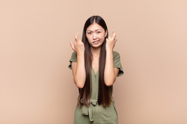 Asian young woman crossing fingers anxiously and hoping for good luck