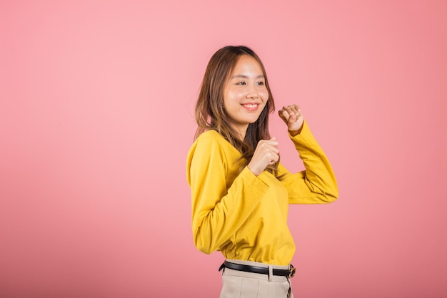 Asian young woman dancing with inspired face expression and raising hands up