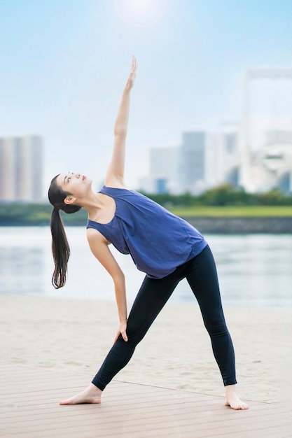 Giovane donna asiatica che fa yoga sulla spiaggia della città