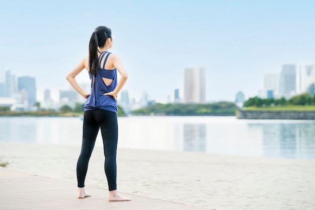 Asian young woman doing yoga on the beach in the city