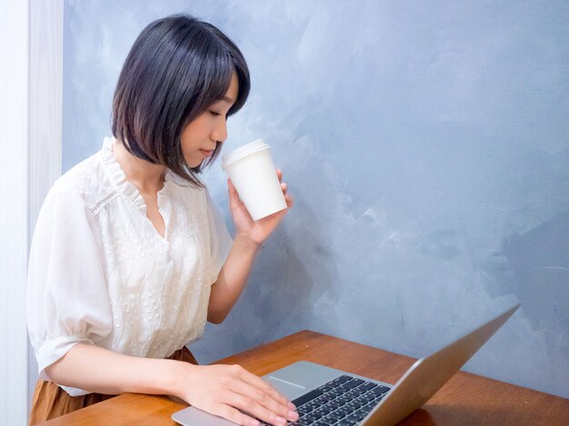 Asian young woman drinks in front of laptop