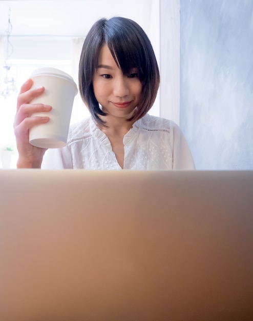 Asian young woman drinks in front of laptop