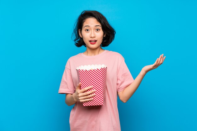 Giovane donna asiatica che mangia i popcorn con espressione facciale colpita