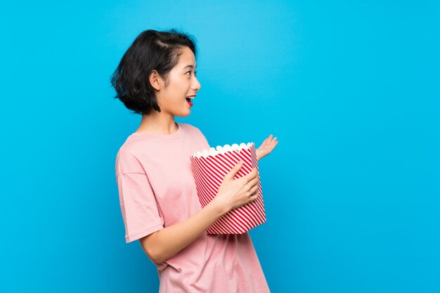 Asian young woman eating popcorns with surprise facial expression