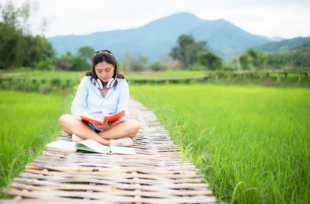 アジアの若い女性は、自然の稲作で木製の橋を読んで楽しむ