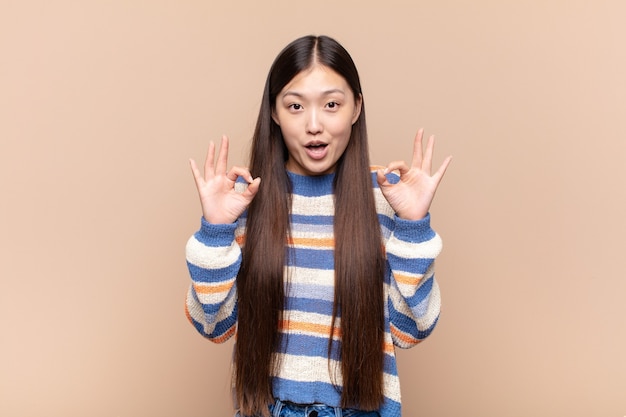 Asian young woman feeling shocked, amazed and surprised, showing approval making okay sign with both hands