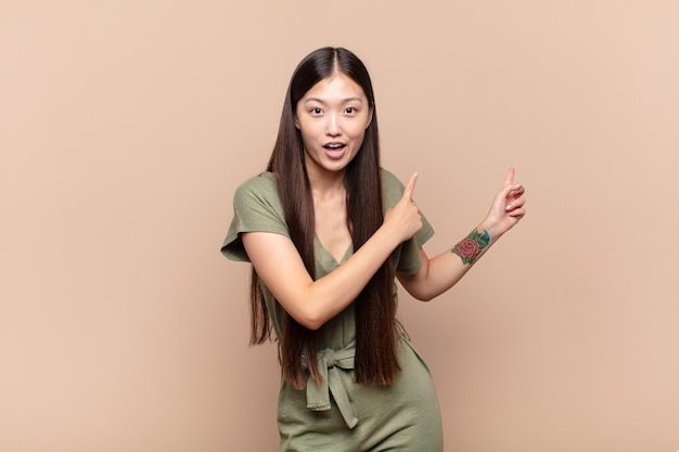 Asian young woman feeling shocked and surprised, pointing to copy space on the side with amazed, open-mouthed look