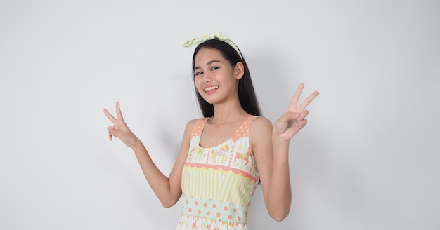 Il gesto asiatico della giovane donna che posa sul fondo bianco rappresenta la rappresentazione allegra e sicura