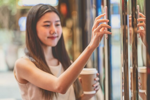 Mano asiatica della giovane donna facendo uso del telefono cellulare che esplora la macchina dei biglietti di film