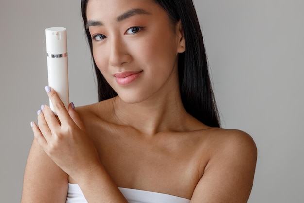 Азиатская молодая женщина держит бутылку косметического крема
