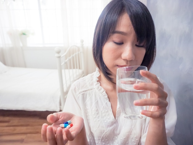 水と錠剤のガラスを保持しているアジアの若い女性。