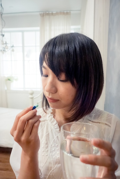 Азиатская молодая женщина, держащая стакан воды и таблетки.