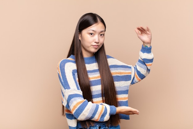 Asian young woman holding an object with both hands on side copy space, showing, offering or advertising an object