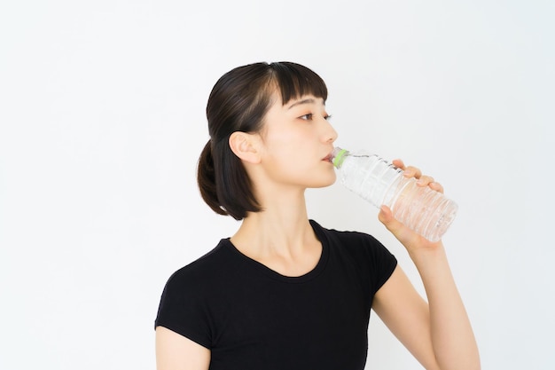 Asian young woman hydrating in sportswear indoors