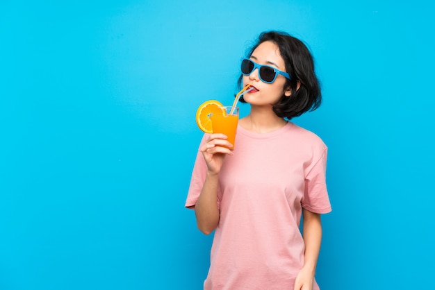 Asian young woman over isolated blue holding a cocktail