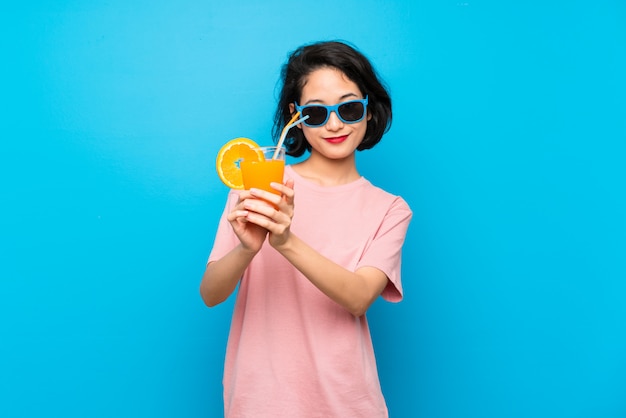 Asian young woman over isolated blue wall holding a cocktail