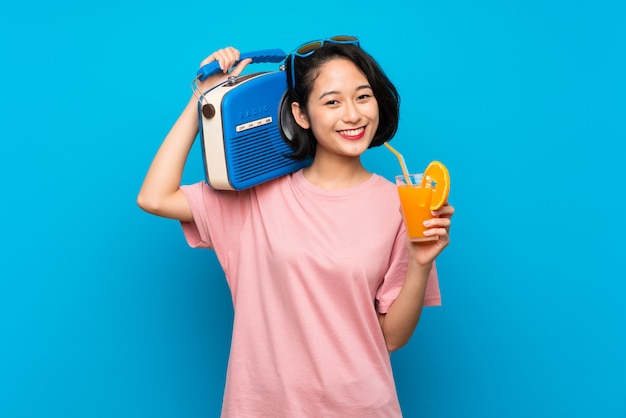 Asian young woman over isolated blue wall holding a radio