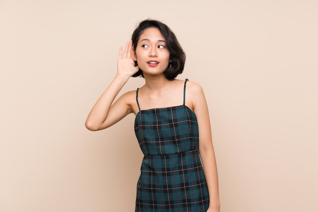 Asian young woman over isolated yellow wall listening to something by putting hand on the ear