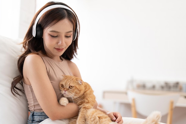 집 침실에서 고양이를 껴안고 헤드폰을 끼고 음악을 듣는 아시아 젊은 여성