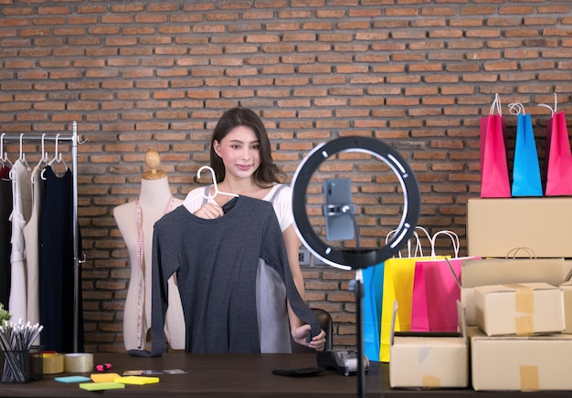 Asian young woman live streaming for sale fashion clothing is blogger presenting for social people. Her is influencer in social online.