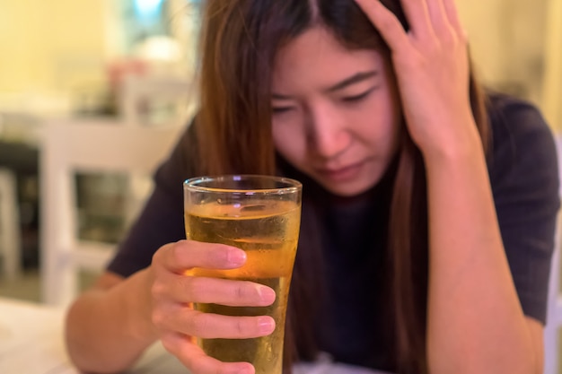 アジアの若い女性が孤独で落ち込んだ行動をし、パブで残りのビールを飲んで