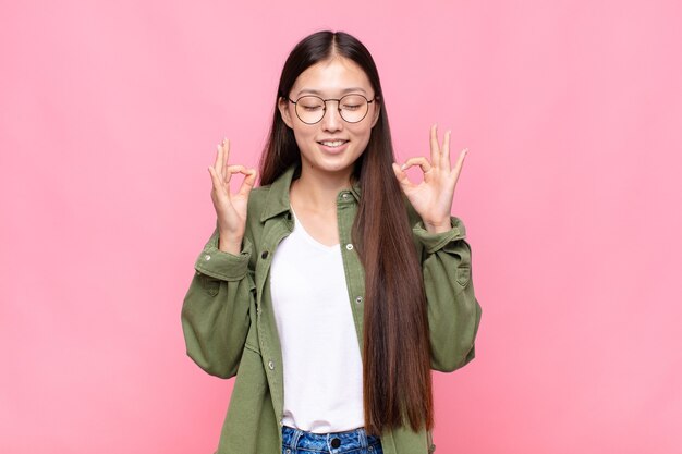 Asian young woman looking concentrated and meditating, feeling satisfied and relaxed, thinking or making a choice