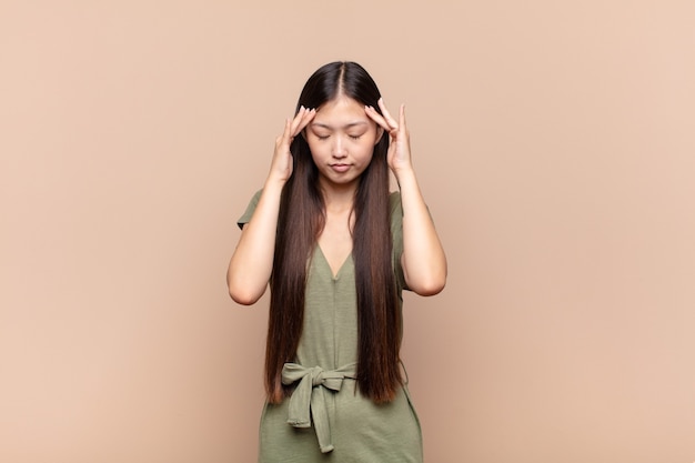 Asian young woman looking concentrated, thoughtful and inspired, brainstorming and imagining with hands on forehead