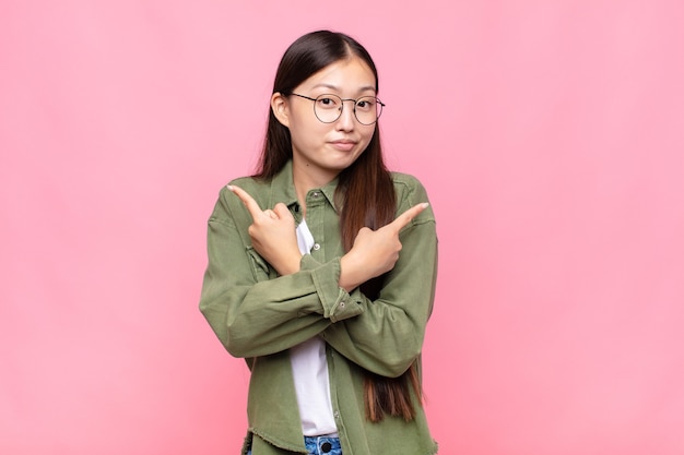 Asian young woman looking puzzled and confused, insecure and pointing in opposite directions with doubts