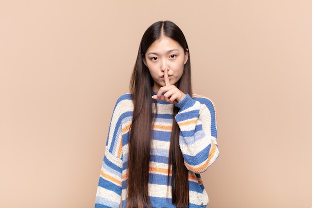 Asian young woman looking serious and cross with finger pressed to lips demanding silence or quiet