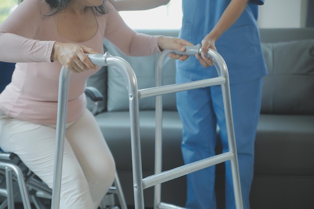 特別養護老人ホームのアジアの若い女性看護師が障害のある老人の世話をする介護士の医師が高齢の高齢患者に理学療法を提供し、裏庭で歩行器や杖で歩く練習をしたり練習したりする