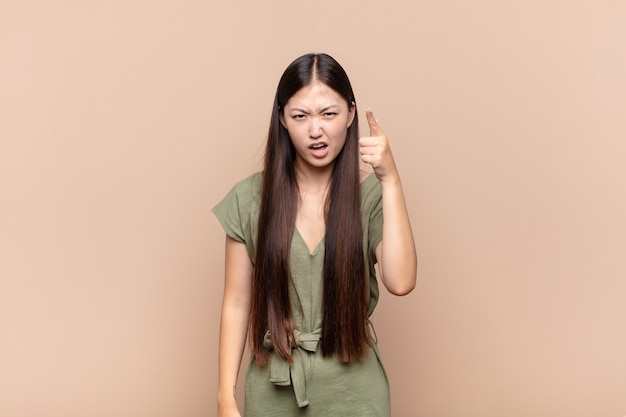 Asian young woman pointing at camera with an angry aggressive expression looking like a furious, crazy boss